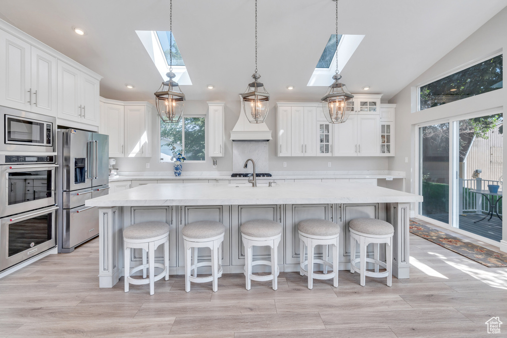 Kitchen with appliances with stainless steel finishes, white cabinetry, a healthy amount of sunlight, and vaulted ceiling with skylight