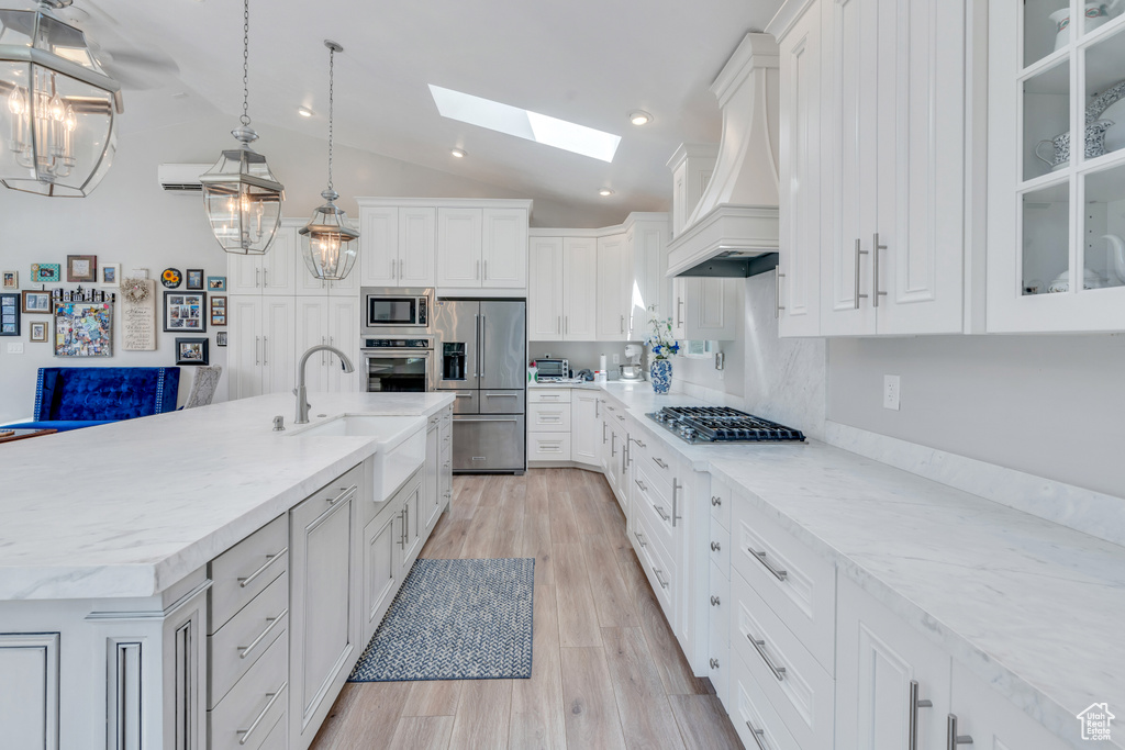 Kitchen with appliances with stainless steel finishes, a center island with sink, sink, premium range hood, and light hardwood / wood-style floors