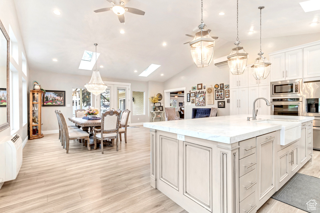 Kitchen featuring ceiling fan, an island with sink, light hardwood / wood-style floors, appliances with stainless steel finishes, and vaulted ceiling with skylight