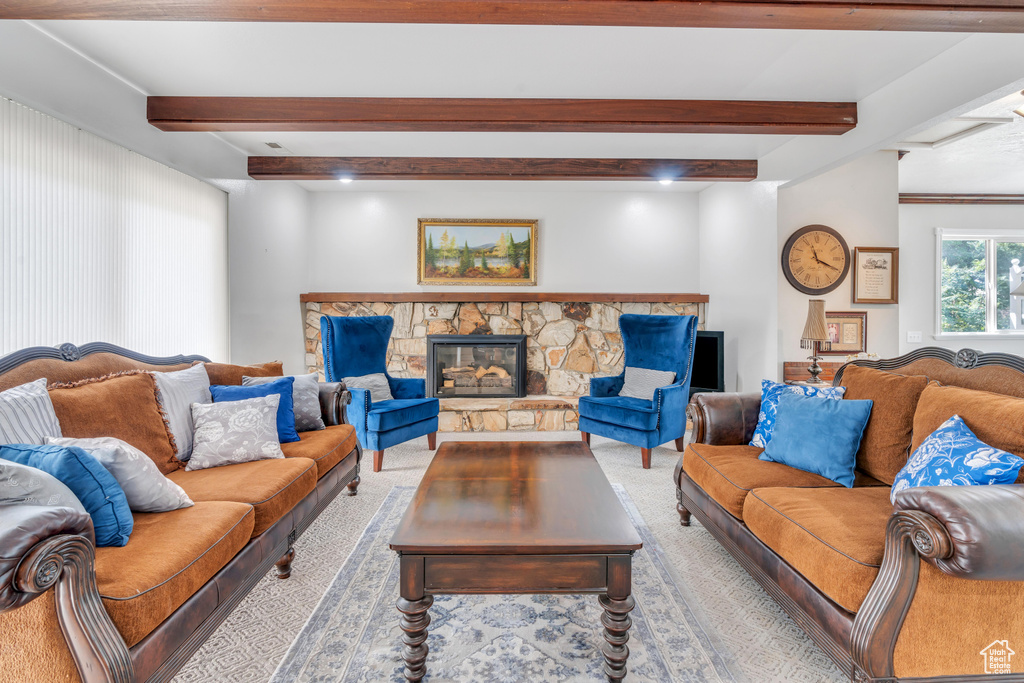 Carpeted living room featuring beam ceiling and a stone fireplace