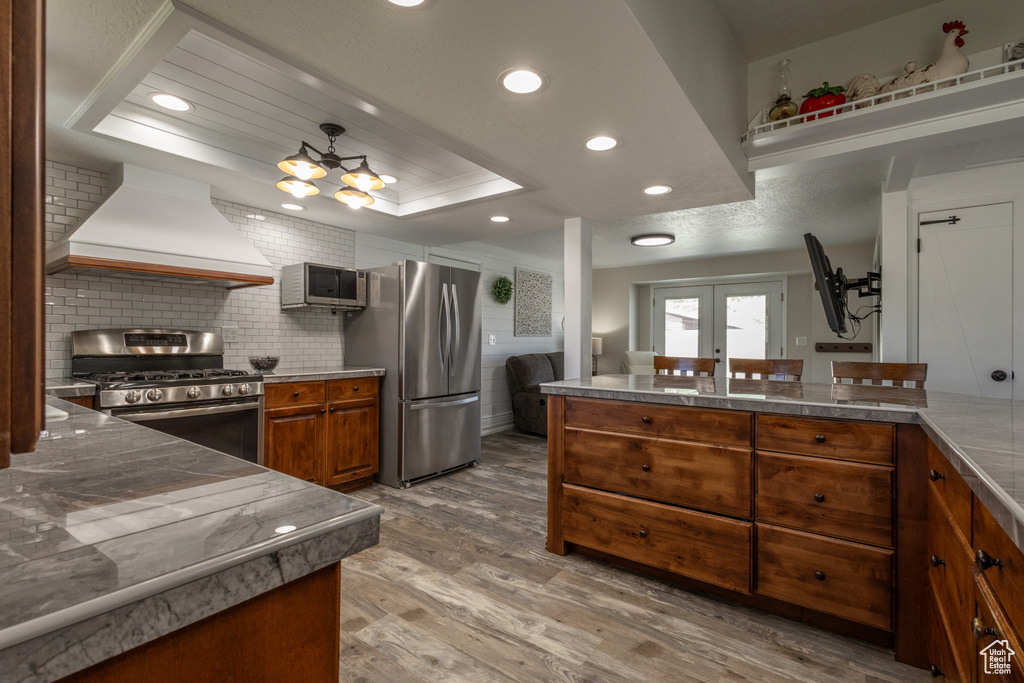 Kitchen featuring appliances with stainless steel finishes, french doors, backsplash, wood-type flooring, and custom range hood