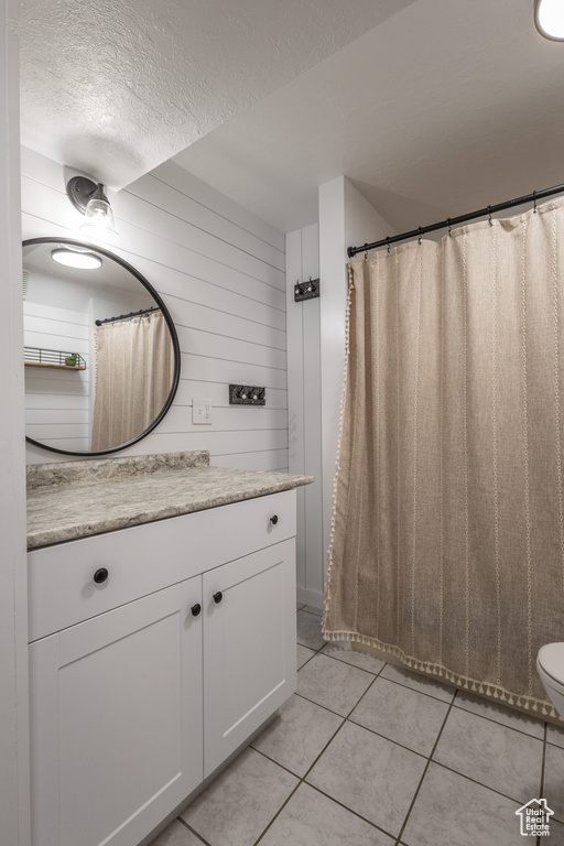 Bathroom featuring wooden walls, a textured ceiling, tile patterned floors, toilet, and vanity