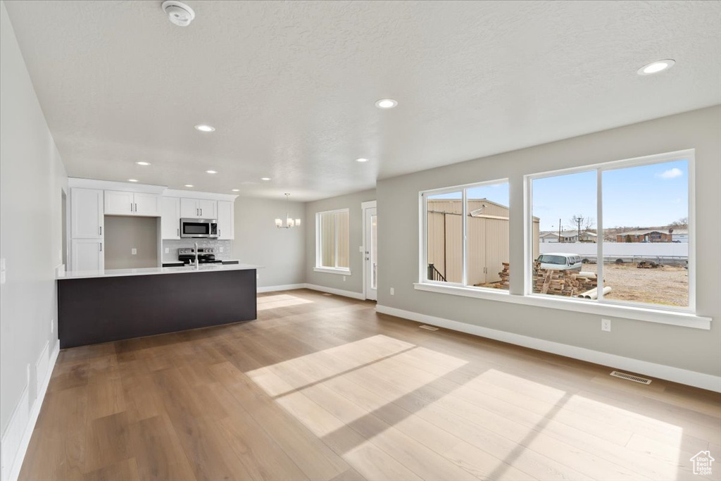 Kitchen with sink, an inviting chandelier, a textured ceiling, light hardwood / wood-style flooring, and white cabinets