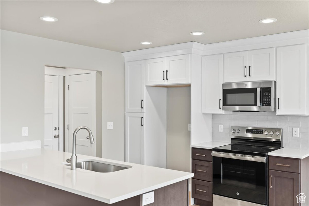 Kitchen with white cabinetry, sink, decorative backsplash, and stainless steel appliances