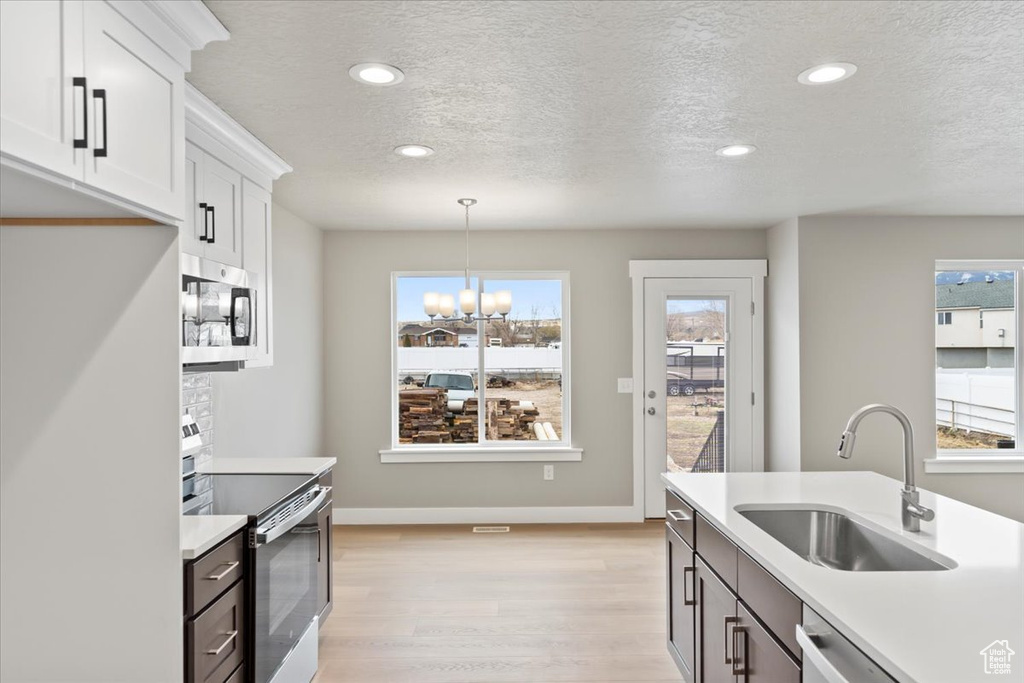 Kitchen with sink, stainless steel appliances, light hardwood / wood-style floors, white cabinets, and decorative light fixtures