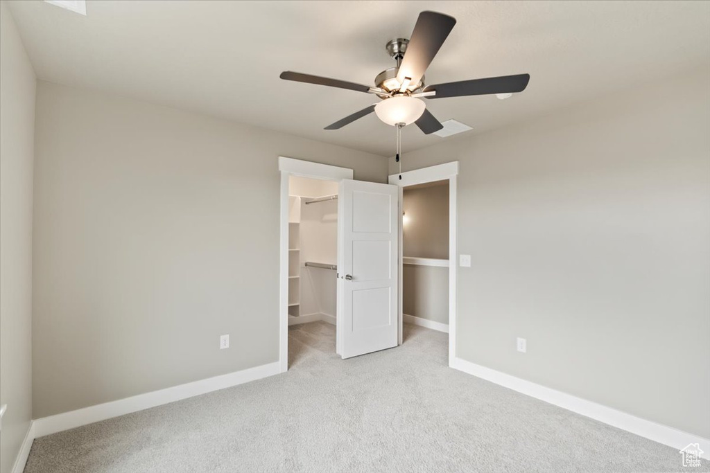 Unfurnished bedroom with light carpet, a walk in closet, a closet, and ceiling fan