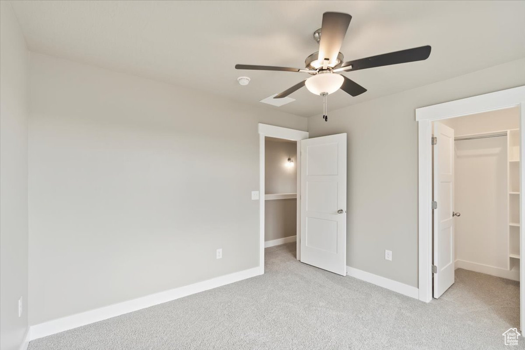 Unfurnished bedroom with ceiling fan, light colored carpet, a spacious closet, and a closet
