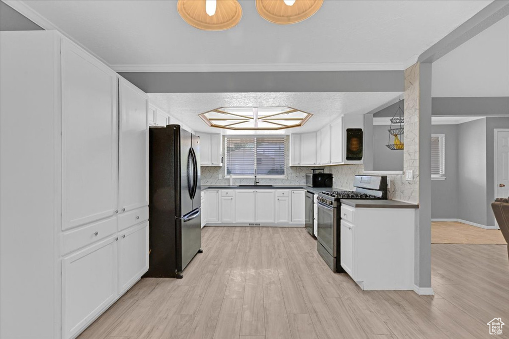 Kitchen with tasteful backsplash, white cabinets, black fridge, light hardwood / wood-style floors, and stainless steel range with gas stovetop