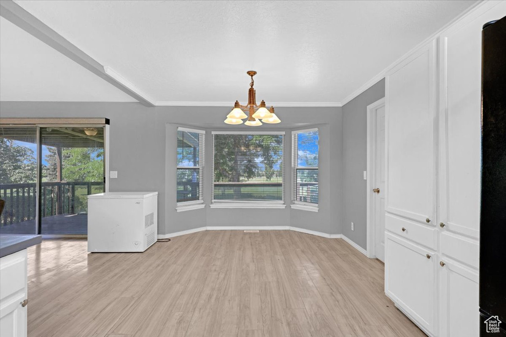 Unfurnished dining area with a notable chandelier, ornamental molding, and light wood-type flooring