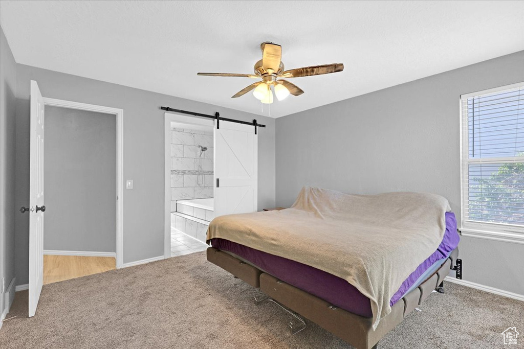 Carpeted bedroom featuring connected bathroom, a barn door, and ceiling fan