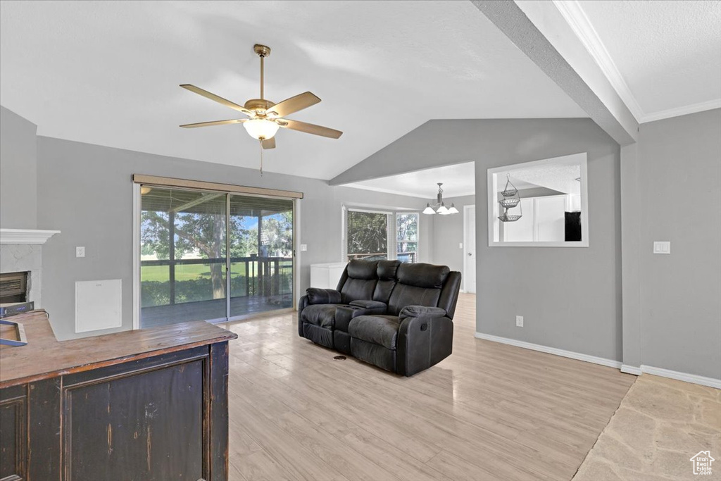 Living room featuring ceiling fan with notable chandelier, a healthy amount of sunlight, light hardwood / wood-style floors, lofted ceiling, and a high end fireplace