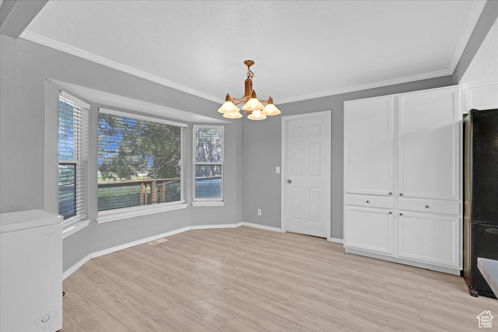 Unfurnished dining area featuring an inviting chandelier, ornamental molding, and light hardwood / wood-style floors