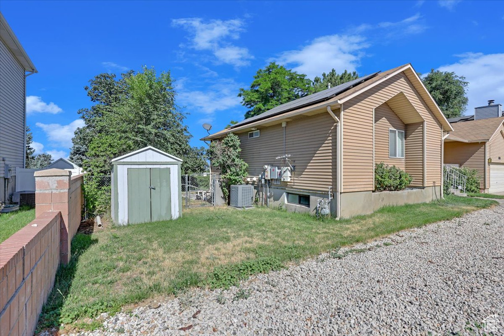 View of property exterior with central air condition unit, a lawn, and a shed