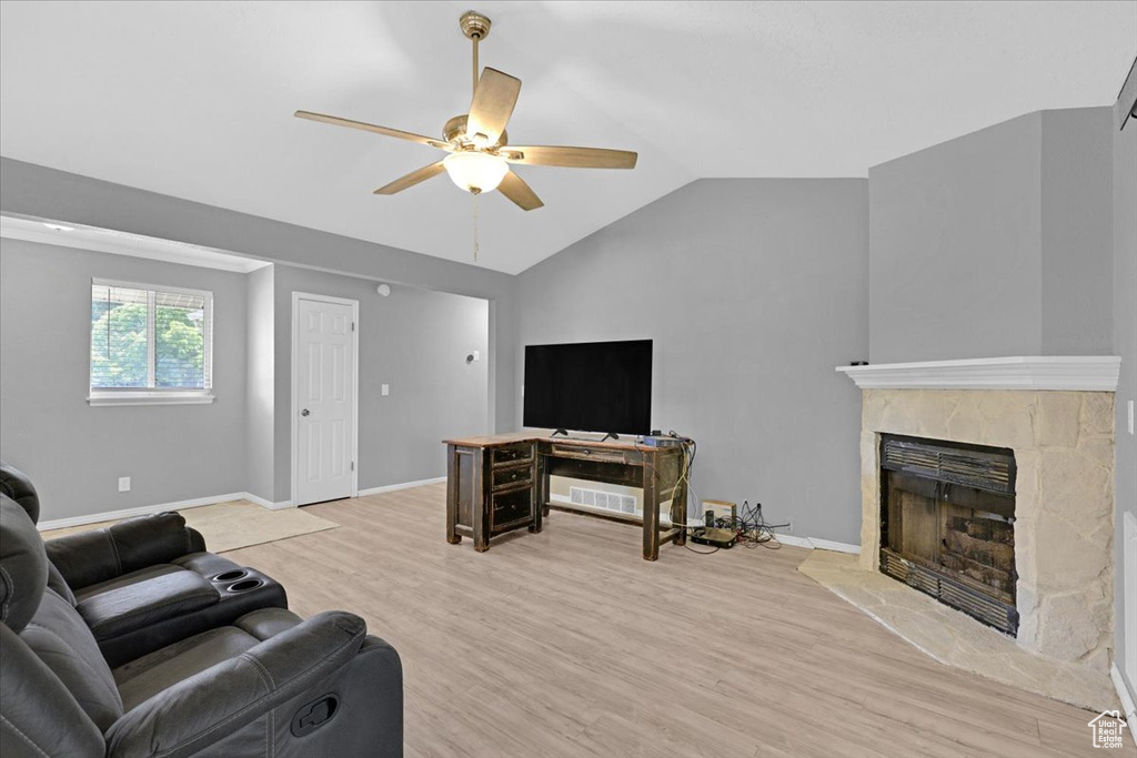 Living room with light hardwood / wood-style floors, a stone fireplace, lofted ceiling, and ceiling fan