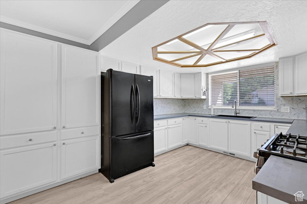 Kitchen with decorative backsplash, light wood-type flooring, sink, and black refrigerator