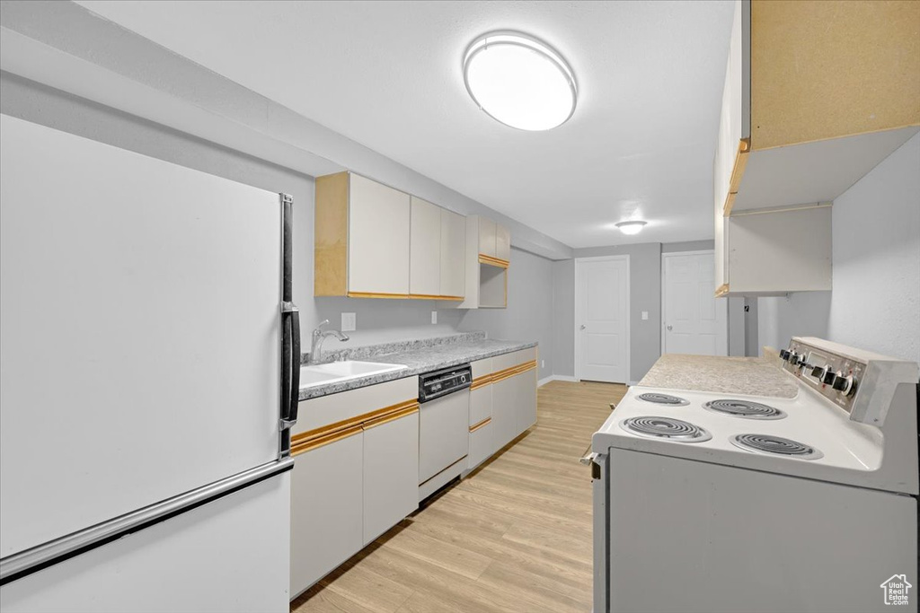 Kitchen with light hardwood / wood-style floors, white appliances, and sink