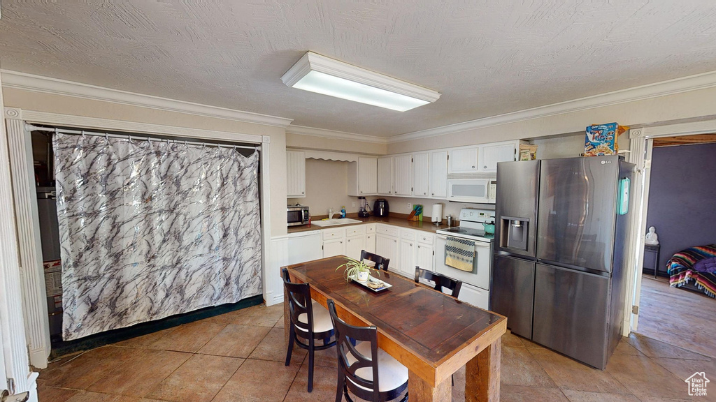 Kitchen featuring white cabinetry, light tile patterned floors, appliances with stainless steel finishes, sink, and ornamental molding