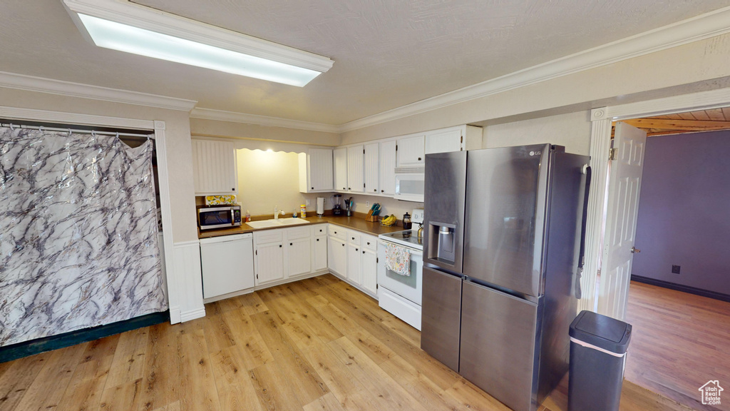 Kitchen featuring light wood-type flooring, ornamental molding, white cabinetry, stainless steel appliances, and sink