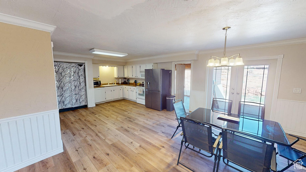 Interior space with white range, stainless steel fridge, pendant lighting, light hardwood / wood-style flooring, and white cabinets