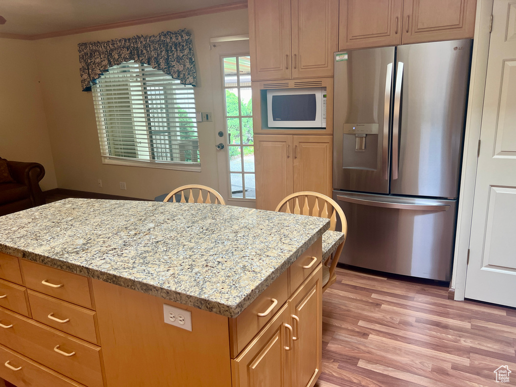 Kitchen with light hardwood / wood-style flooring, light stone countertops, white microwave, and stainless steel fridge