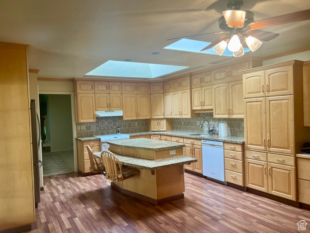 Kitchen with a skylight, white appliances, hardwood / wood-style floors, and a kitchen island