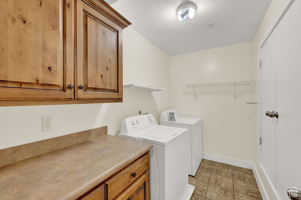 Laundry room featuring separate washer and dryer, cabinets, light tile patterned floors, and a textured ceiling