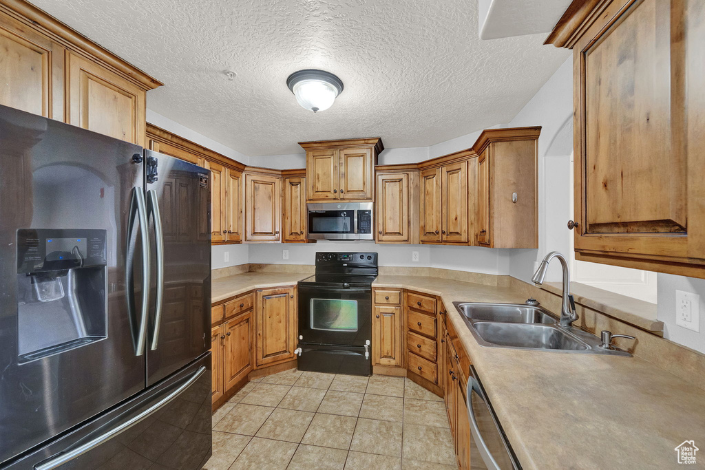 Kitchen featuring light tile patterned floors, black appliances, sink, and a textured ceiling