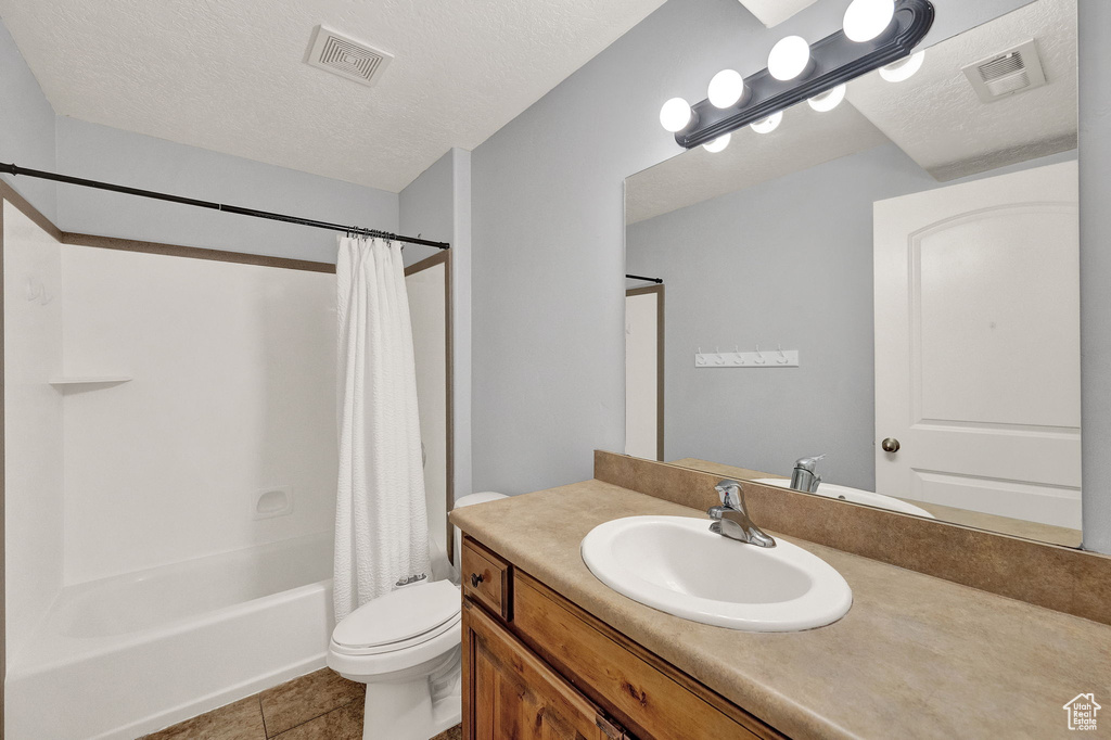 Full bathroom with shower / bath combo with shower curtain, a textured ceiling, tile patterned floors, toilet, and vanity