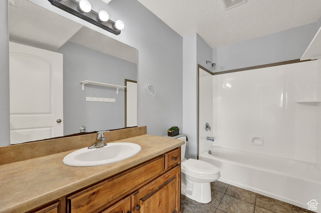 Full bathroom with a textured ceiling, bathtub / shower combination, toilet, vanity, and tile patterned floors