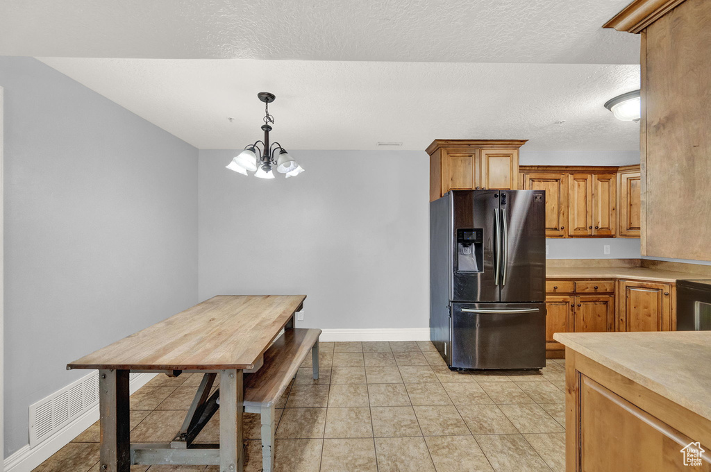 Kitchen with light tile patterned floors, a textured ceiling, an inviting chandelier, decorative light fixtures, and stainless steel refrigerator with ice dispenser