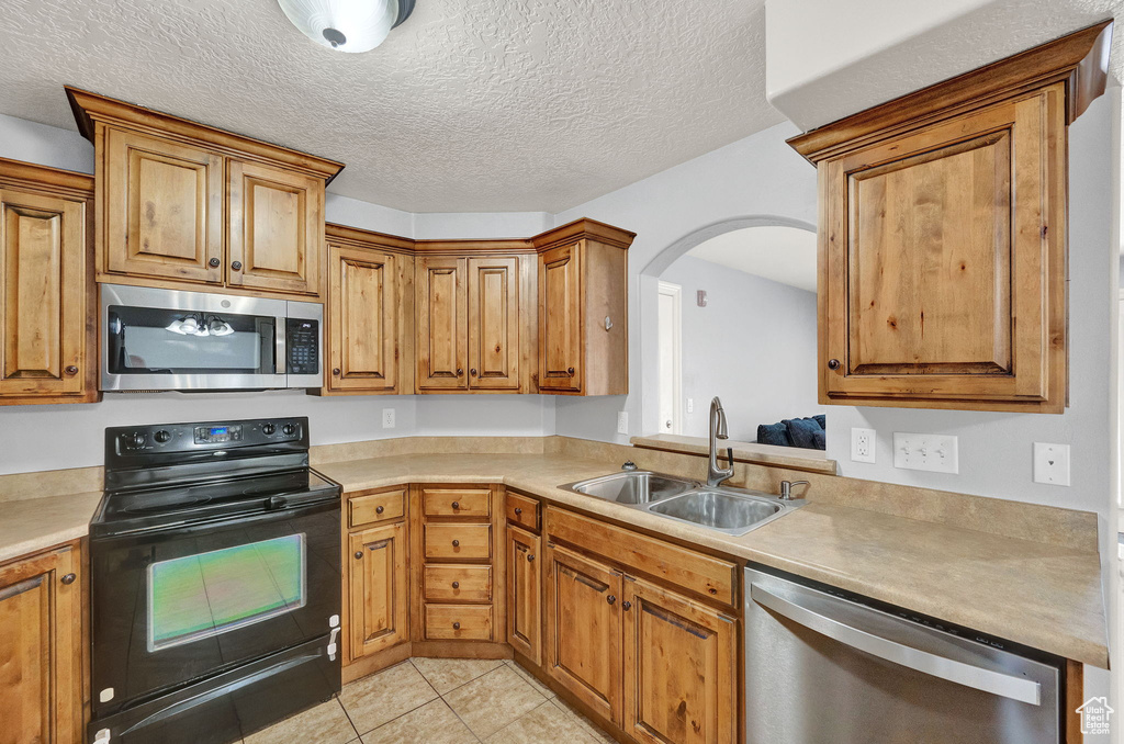 Kitchen featuring light tile patterned floors, appliances with stainless steel finishes, sink, and a textured ceiling