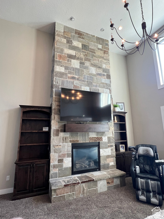 Living room with an inviting chandelier, a fireplace, a textured ceiling, and dark colored carpet