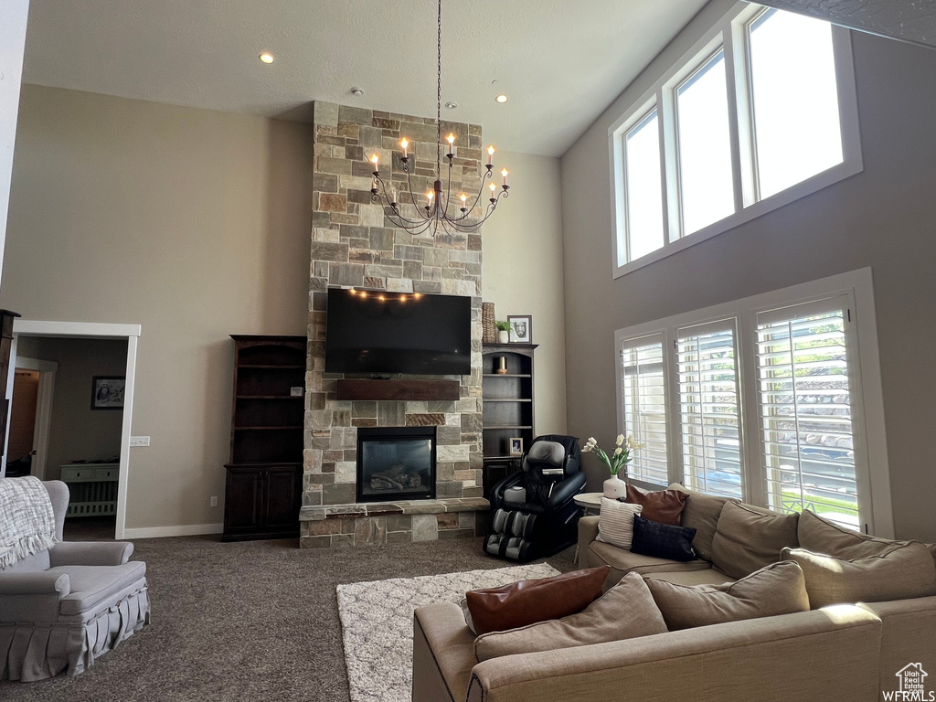 Carpeted living room featuring a stone fireplace, a chandelier, and a towering ceiling