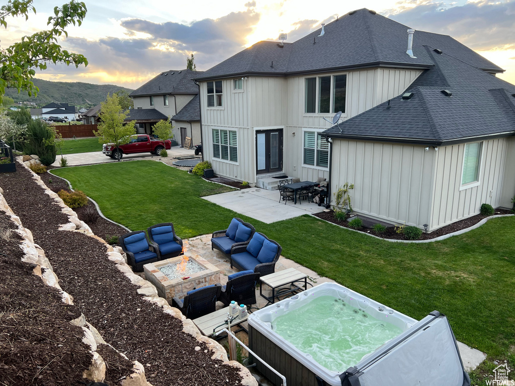 Back house at dusk featuring a hot tub, a patio area, a lawn, and outdoor lounge area