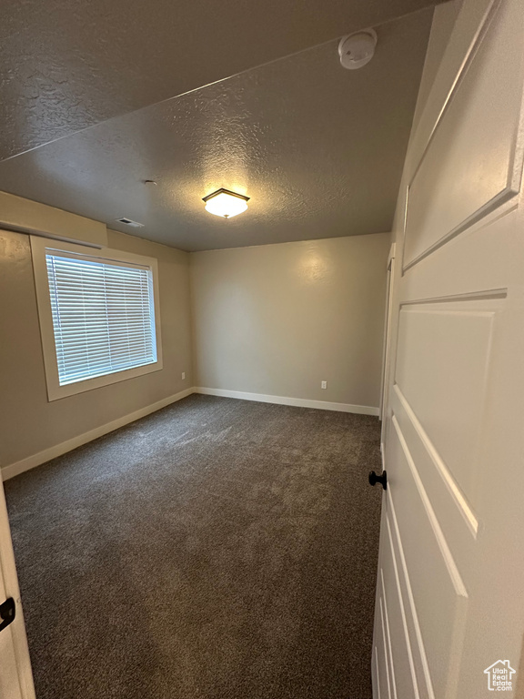 Empty room with baseboards, dark colored carpet, and a textured ceiling