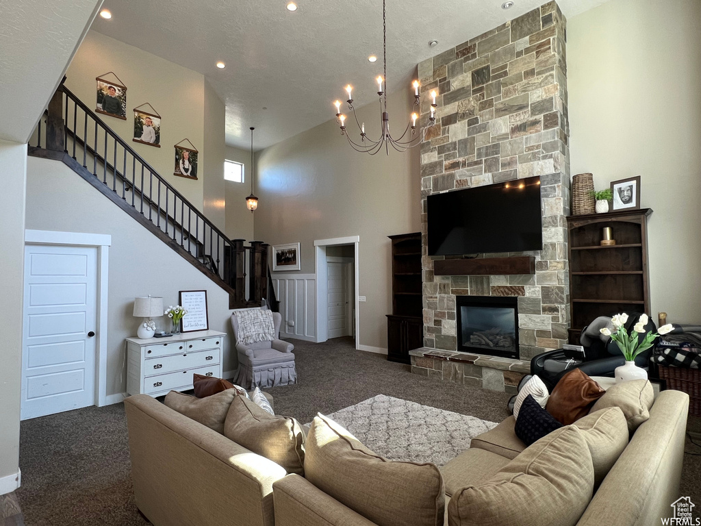 Living room with a chandelier, a textured ceiling, a high ceiling, dark colored carpet, and a fireplace