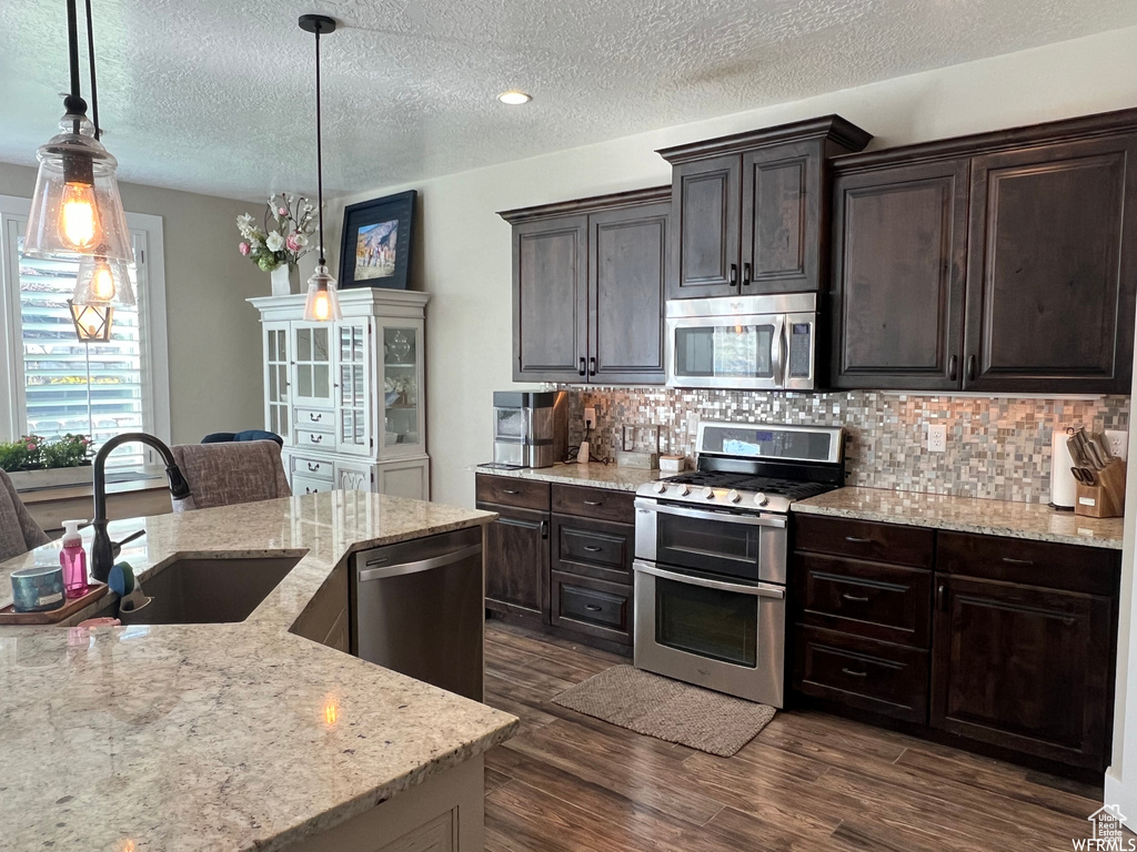 Kitchen featuring hanging light fixtures, sink, appliances with stainless steel finishes, backsplash, and dark wood-type flooring