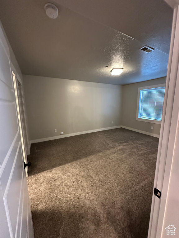 Unfurnished bedroom featuring a textured ceiling, baseboards, visible vents, and dark carpet