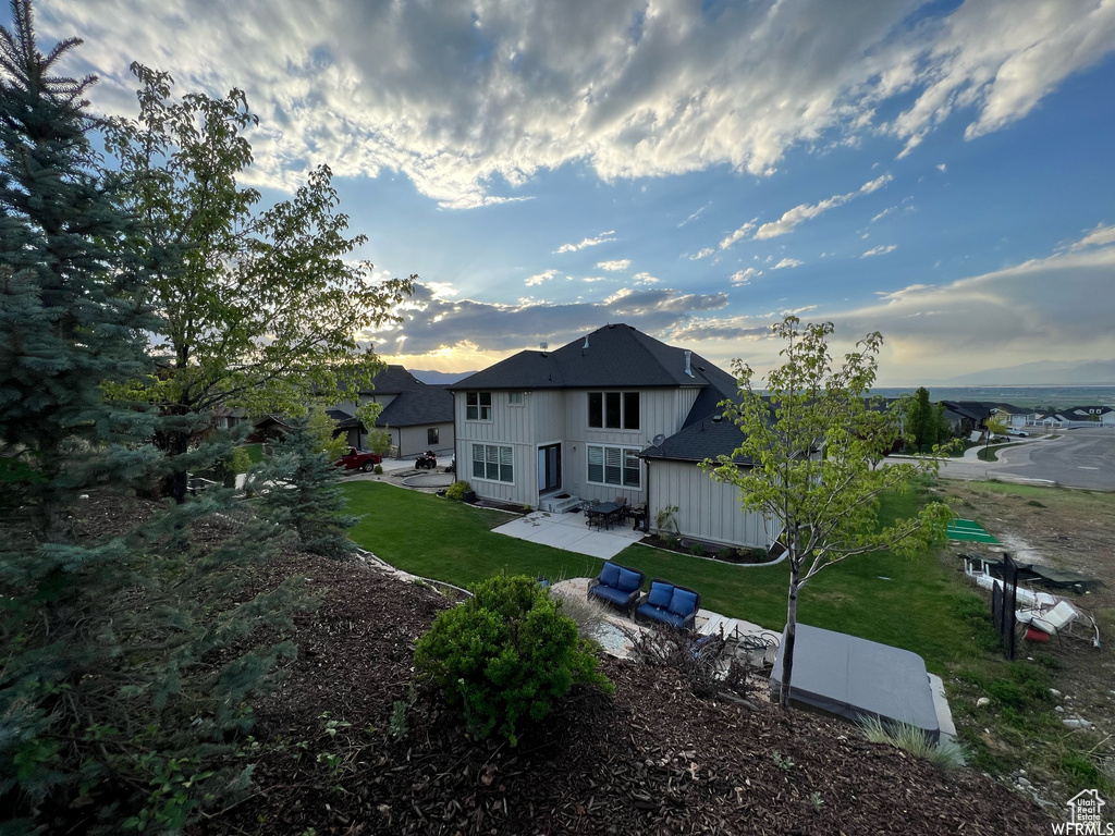 Back house at dusk with a lawn and a patio area