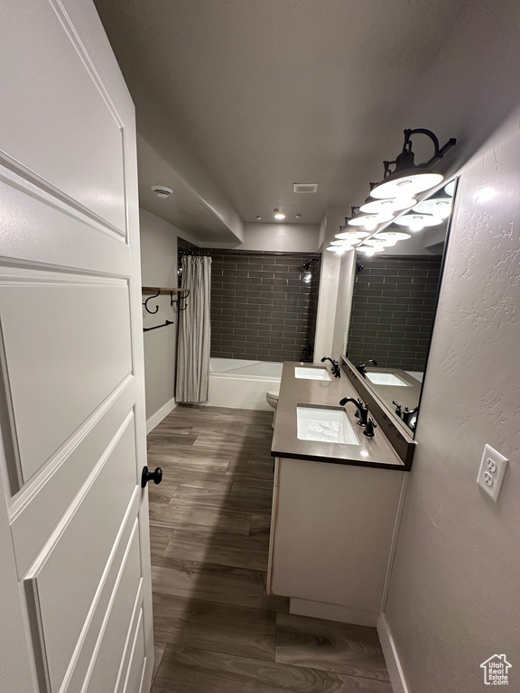 Bathroom featuring toilet, wood finished floors, vanity, baseboards, and shower / tub combo