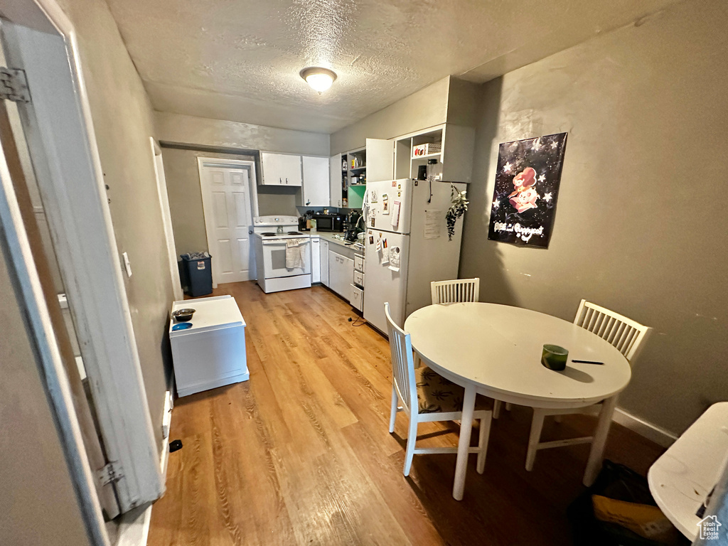 Kitchen with light hardwood / wood-style flooring, white appliances, a textured ceiling, and white cabinetry