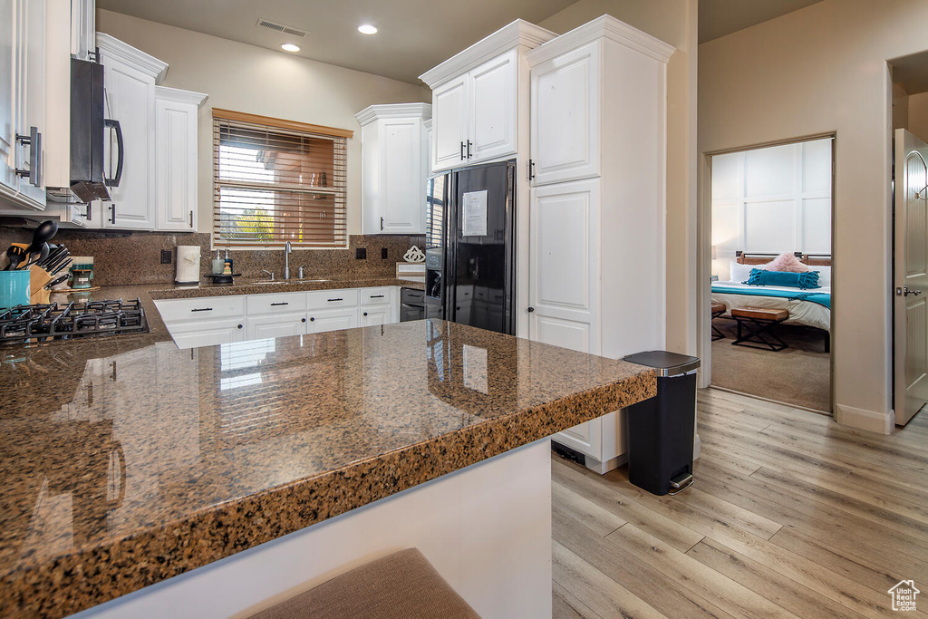 Kitchen with black appliances, white cabinets, decorative backsplash, light carpet, and kitchen peninsula