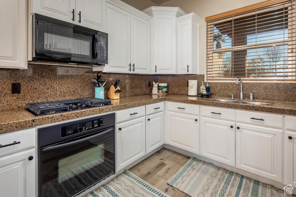 Kitchen featuring black appliances, tasteful backsplash, white cabinets, sink, and light hardwood / wood-style flooring