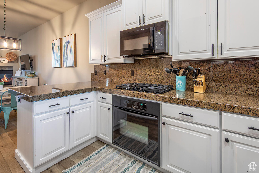 Kitchen featuring tasteful backsplash, black appliances, pendant lighting, light wood-type flooring, and white cabinetry