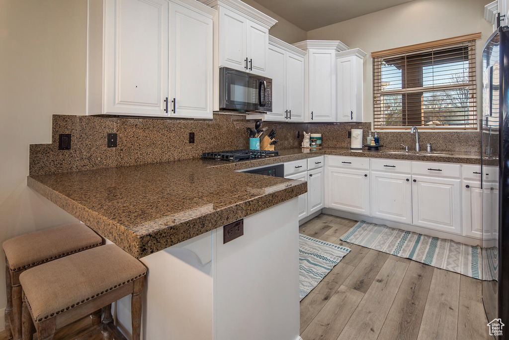 Kitchen with a breakfast bar, light hardwood / wood-style flooring, tasteful backsplash, white cabinets, and sink