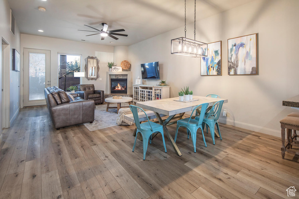 Dining area featuring ceiling fan with notable chandelier, wood-type flooring, and a tile fireplace