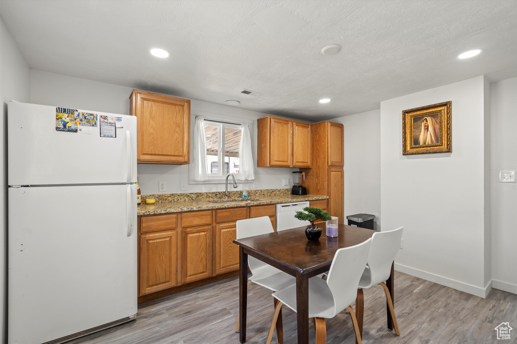 Kitchen with sink, light stone countertops, light wood-type flooring, and white appliances