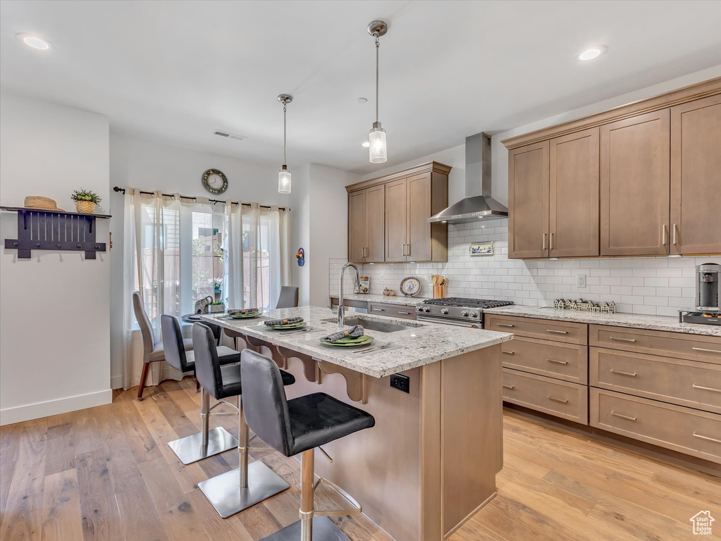 Kitchen with light hardwood / wood-style flooring, tasteful backsplash, wall chimney range hood, hanging light fixtures, and sink