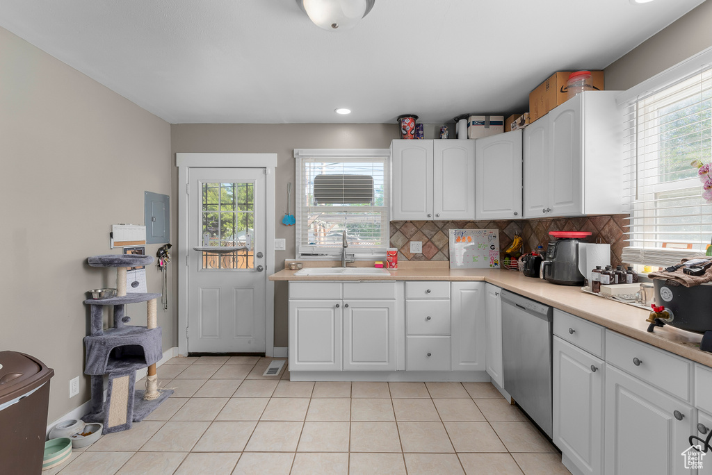 Kitchen featuring light tile patterned flooring, white cabinets, stainless steel dishwasher, decorative backsplash, and sink