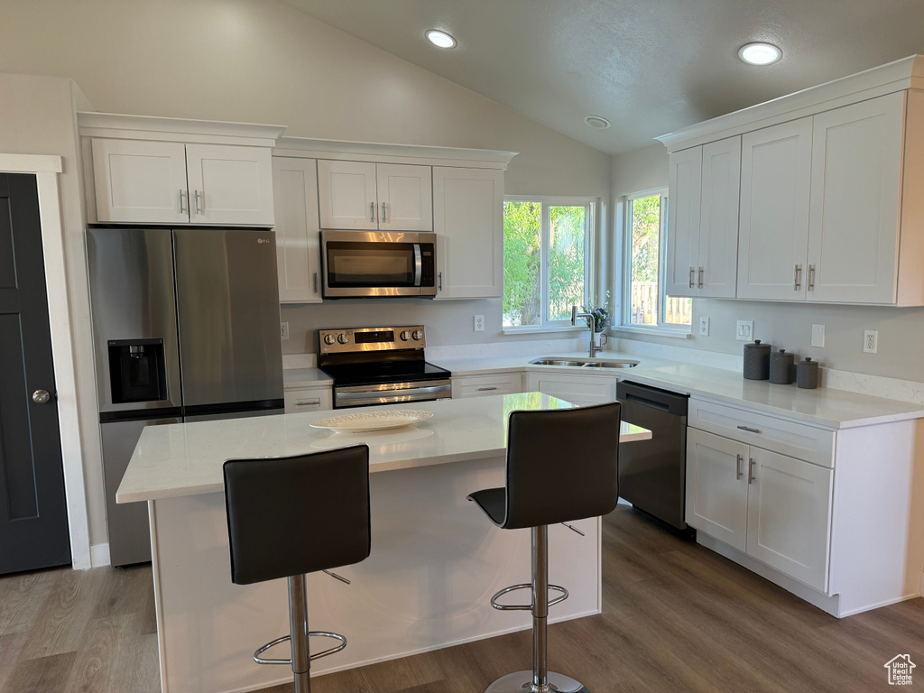 Kitchen featuring white cabinetry, hardwood / wood-style flooring, stainless steel appliances, a center island, and lofted ceiling